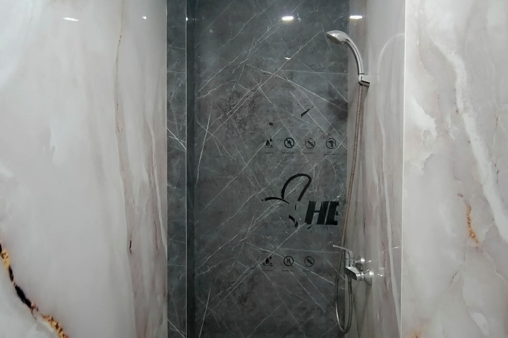 Un baño con ducha envuelta en cristal, paredes de mármol e indicador de flujo de agua visible.