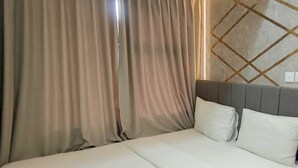 A hotel room with a bed, curtains, a headboard, and a wall with a geometric pattern. - Functional And Cozy 2Br Apartment At Vida View Makassar (Makassar)