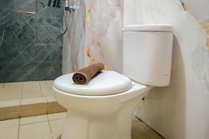 Lavabo amb una tovallola a la part superior, zona de dutxa amb porta de vidre i paret de marbre.