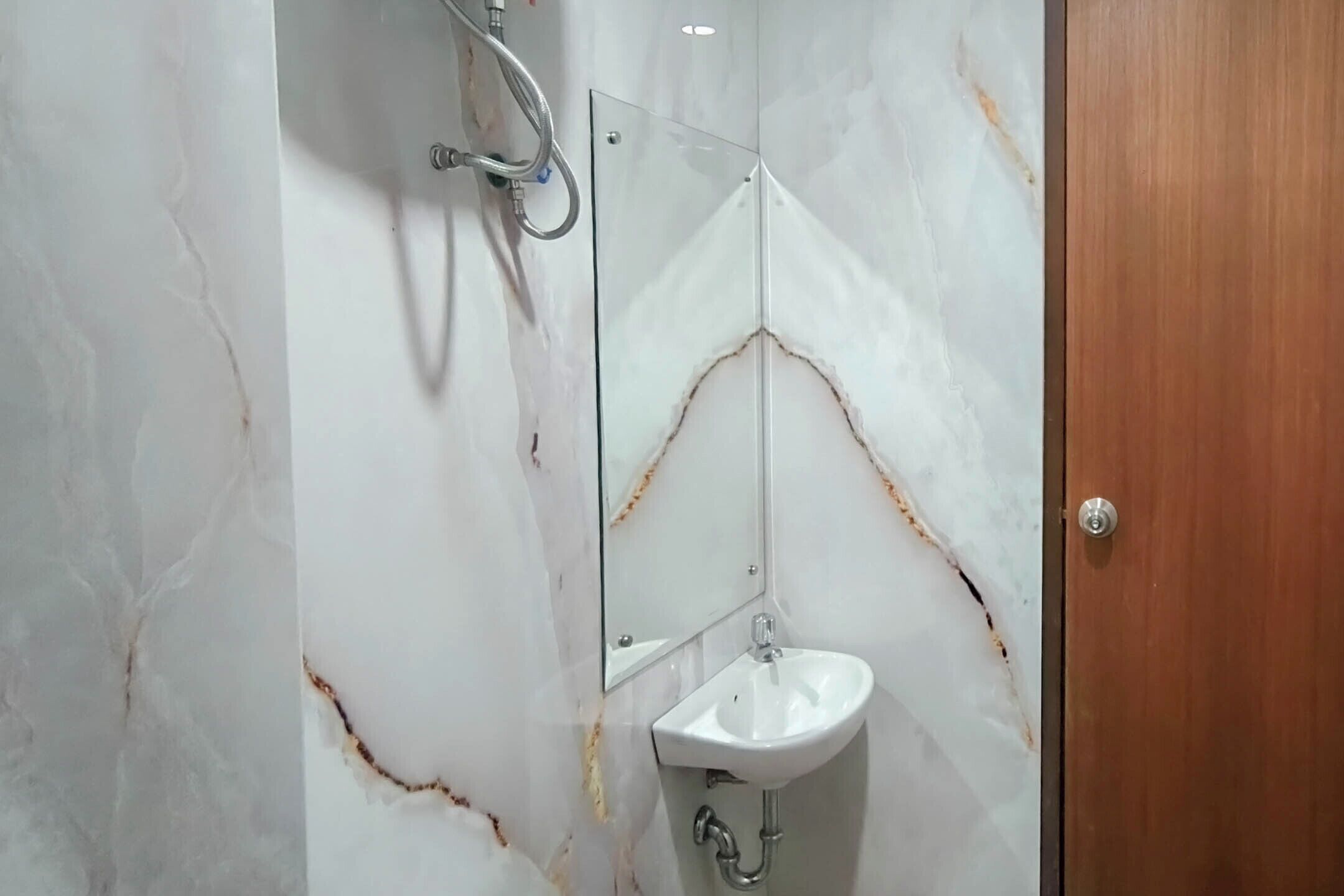 A bathroom with a marble wall, a glass shower enclosure, and a wooden door.