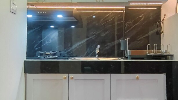 A modern kitchen with a black countertop, a sink, and a range hood. - Functional And Cozy 2Br Apartment At Vida View Makassar (Makassar)