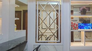 A modern interior with a decorative metal partition, a television displaying a floral image, and a marble wall. - Functional And Cozy 2Br Apartment At Vida View Makassar (Makassar)