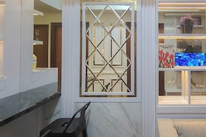 A modern interior with a decorative metal partition, a television displaying a floral image, and a marble wall. - Functional And Cozy 2Br Apartment At Vida View Makassar (Makassar)