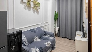 A modern living room with a sofa, a small table, a plant, and a TV stand. - Cozy Living 2Br At Vida View Makassar Apartment (Makassar)