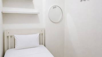A white bed with a pillow, a round mirror, and a coat rack on a plain wall.