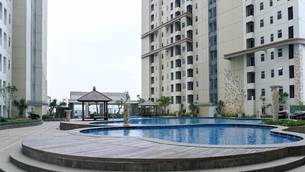 A swimming pool surrounded by a wooden deck, with high-rise residential buildings in the background. - Good Choice And Homey Studio Apartment Vittoria Residence (Jakarta)