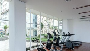 A gym with exercise equipment, large windows, and a view of buildings outside. - Good Choice And Homey Studio Apartment Vittoria Residence (Jakarta)