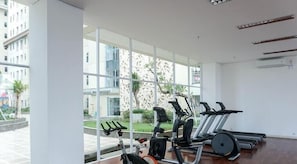A gym with exercise equipment, large windows, and a view of buildings outside. - Good Choice And Homey Studio Apartment Vittoria Residence (Jakarta)
