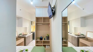 A hotel room with a large mirror, a TV mounted on the wall, a bed with a green bedspread, and a small desk with a chair. - Good Choice And Homey Studio Apartment Vittoria Residence (Jakarta)