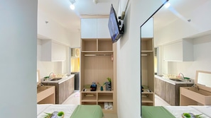A hotel room with a large mirror, a TV mounted on the wall, a bed with a green bedspread, and a small desk with a chair. - Good Choice And Homey Studio Apartment Vittoria Residence (Jakarta)