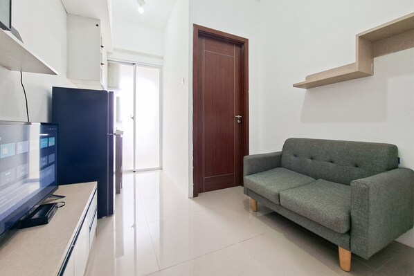 Ein modernes Wohnzimmer mit Fernseher, grauem Sofa, Holztür und weißer Wand.