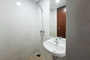 Ein Badezimmer mit weißen Fliesen, einem Waschbecken, einer Dusche und einer Holztür.
