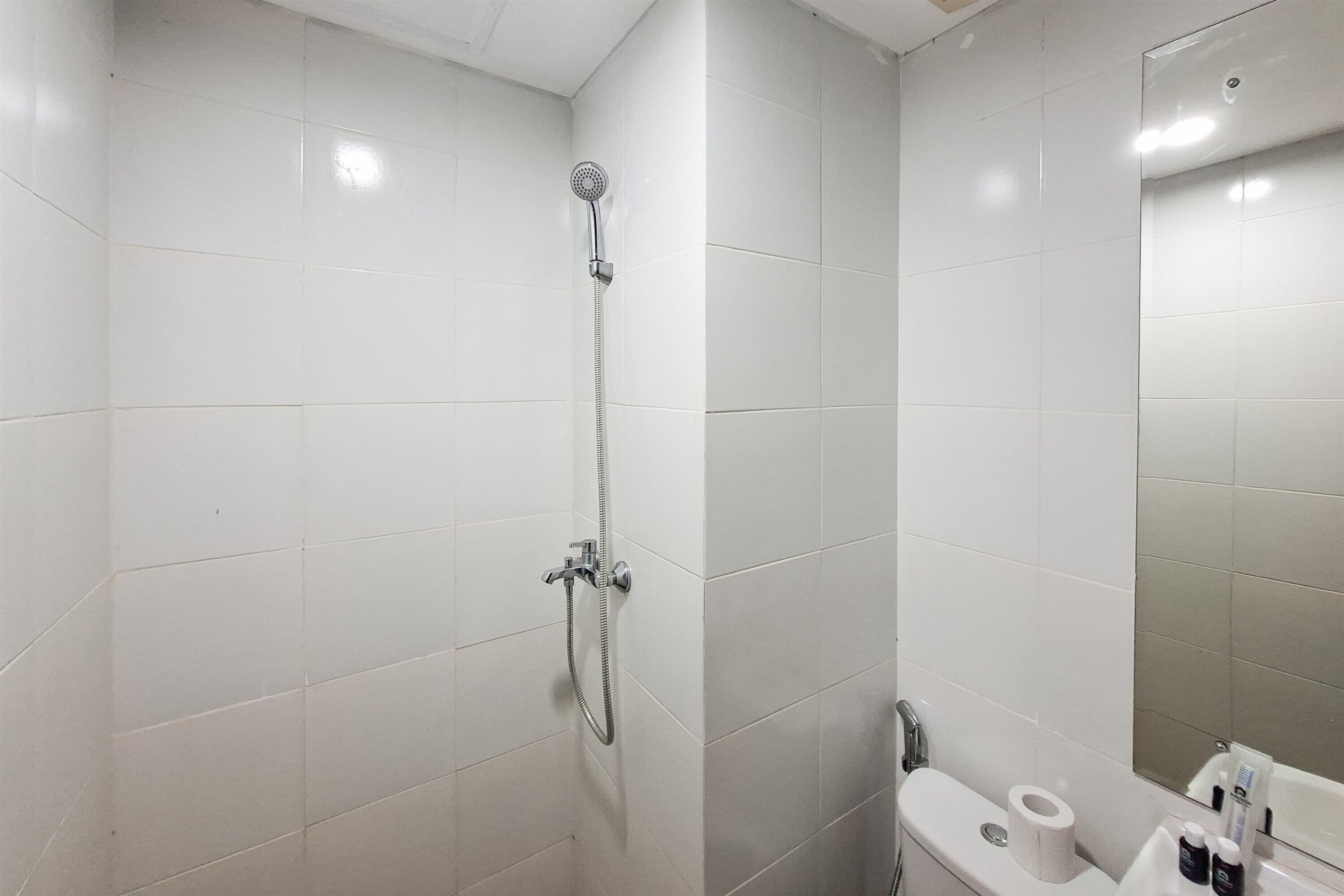 Een badkamer met witte tegels, een douche, toilet en een spiegel.