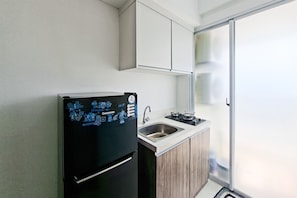 Eine kompakte Küche mit Kühlschrank, Spüle und Herd, sowie eine Glastür zum Balkon.