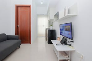 Ein modernes Wohnzimmer mit einer Couch, einem Fernseher, einem Schreibtisch mit Computer und einem Kühlschrank.