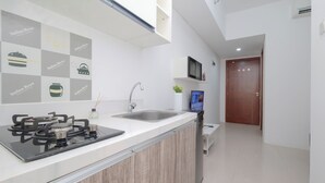 A modern kitchen with a gas stove, sink, and a wall-mounted TV. - Tranquil 1Br For 2 Pax At Vittoria Residence (Jakarta)
