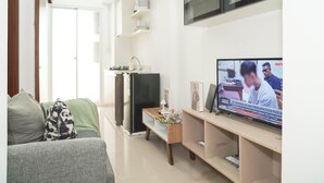 A living room with a sofa, a TV, a kitchen area, and a door leading to another room. - Homey And Best Place 2Br At Apartment Vittoria Residence (Jakarta)
