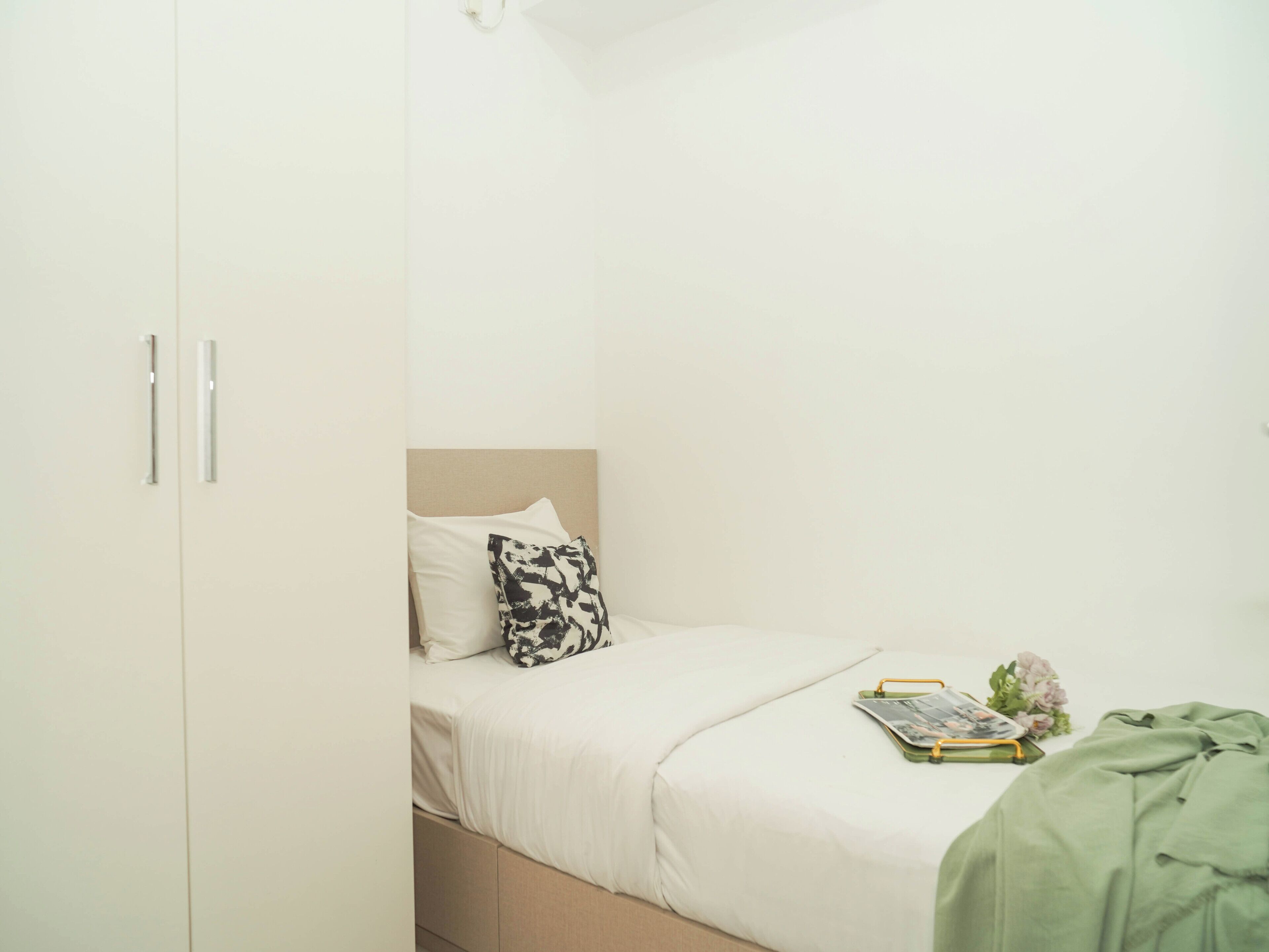 A bedroom with a bed, a pillow, a green blanket, and a magazine on the bed.
