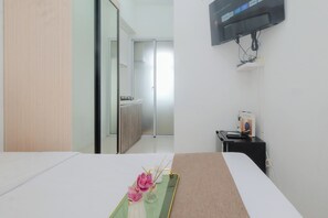 A hotel room with a bed, a small table with a tray, a TV mounted on the wall, and a door leading to a bathroom. - 1 Pax Functional Studio At Vittoria Residence (Jakarta)