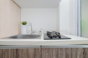 A modern kitchen with a stainless steel sink, a gas stove, and a small potted plant on the countertop. - 1 Pax Functional Studio At Vittoria Residence (Jakarta)
