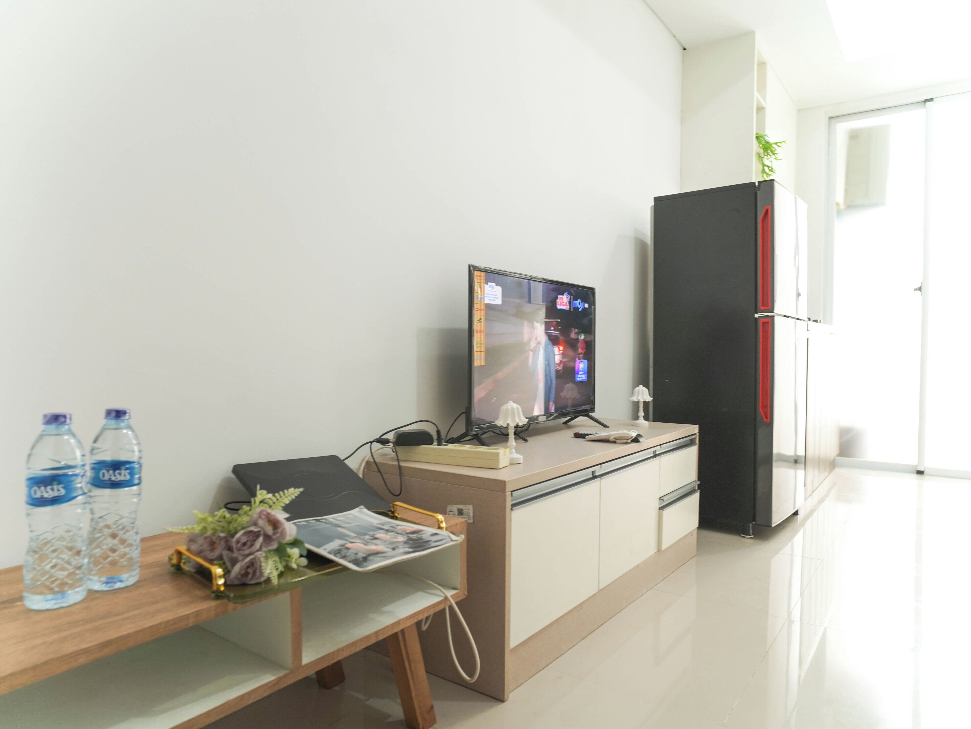 A modern kitchen with a refrigerator, a television, and a wooden table with water bottles and a magazine.