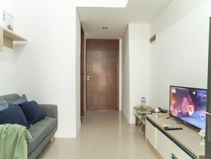 Ein Wohnzimmer mit einer Couch, einem Fernseher, einem kleinen Tisch mit einer Fernbedienung und einer Tür zu einem weiteren Raum.