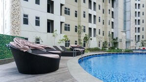 A swimming pool with lounge chairs and a wooden deck, surrounded by a building with multiple windows and balconies. - Affordable Price And Homey 1Br Apartment At Vittoria Residence (Jakarta)