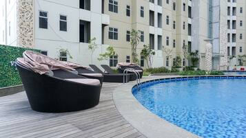 A swimming pool with lounge chairs and a wooden deck, surrounded by a building with multiple windows and balconies.
