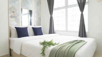 A bedroom with a bed, pillows, a green plant, and curtains.