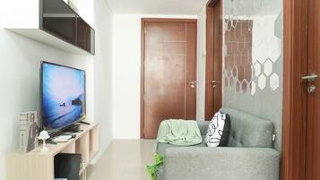 A living room with a flat-screen TV, a sofa, a wooden cabinet, and a door with a geometric-patterned glass panel.