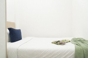 Ein Bett mit weißer Bettwäsche, einem blauen Kissen und einer grünen Decke.