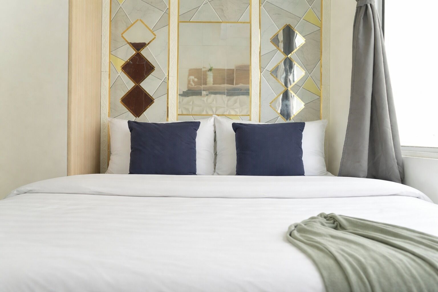 Ein Hotelzimmer mit einem Bett, zwei Kissen, einer Decke und einem Fenster mit Vorhängen.