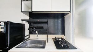 A modern kitchen with a stainless steel sink, black cabinets, and a gas stove. - Good And Restful 1Br At Apartment Vittoria Residence (Jakarta)