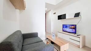 A modern living room with a grey sofa, a wooden coffee table, and a flat-screen TV on a white cabinet. - Good And Restful 1Br At Apartment Vittoria Residence (Jakarta)
