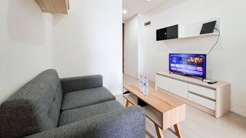 A modern living room with a grey sofa, a wooden coffee table, and a flat-screen TV on a white cabinet.