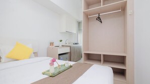 Ein Hotelzimmer mit Bett, Nachttisch mit Tablett, einer kleinen Küchenzeile und einem Kleiderschrank.