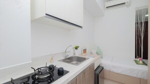A compact kitchen with a gas stove, sink, and a window with curtains. - Homey And Minimalist Studio Room At Apartment Vittoria Residence (Jakarta)