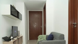 A small, narrow room with a grey sofa, a television on a stand, and a wooden door. - Cozy And Good 2Br At Apartment Vittoria Residence (Jakarta)