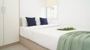 A minimalist bedroom with a bed, white walls, a window, and a green plant on the bed. - Cozy And Good 2Br At Apartment Vittoria Residence (Jakarta)