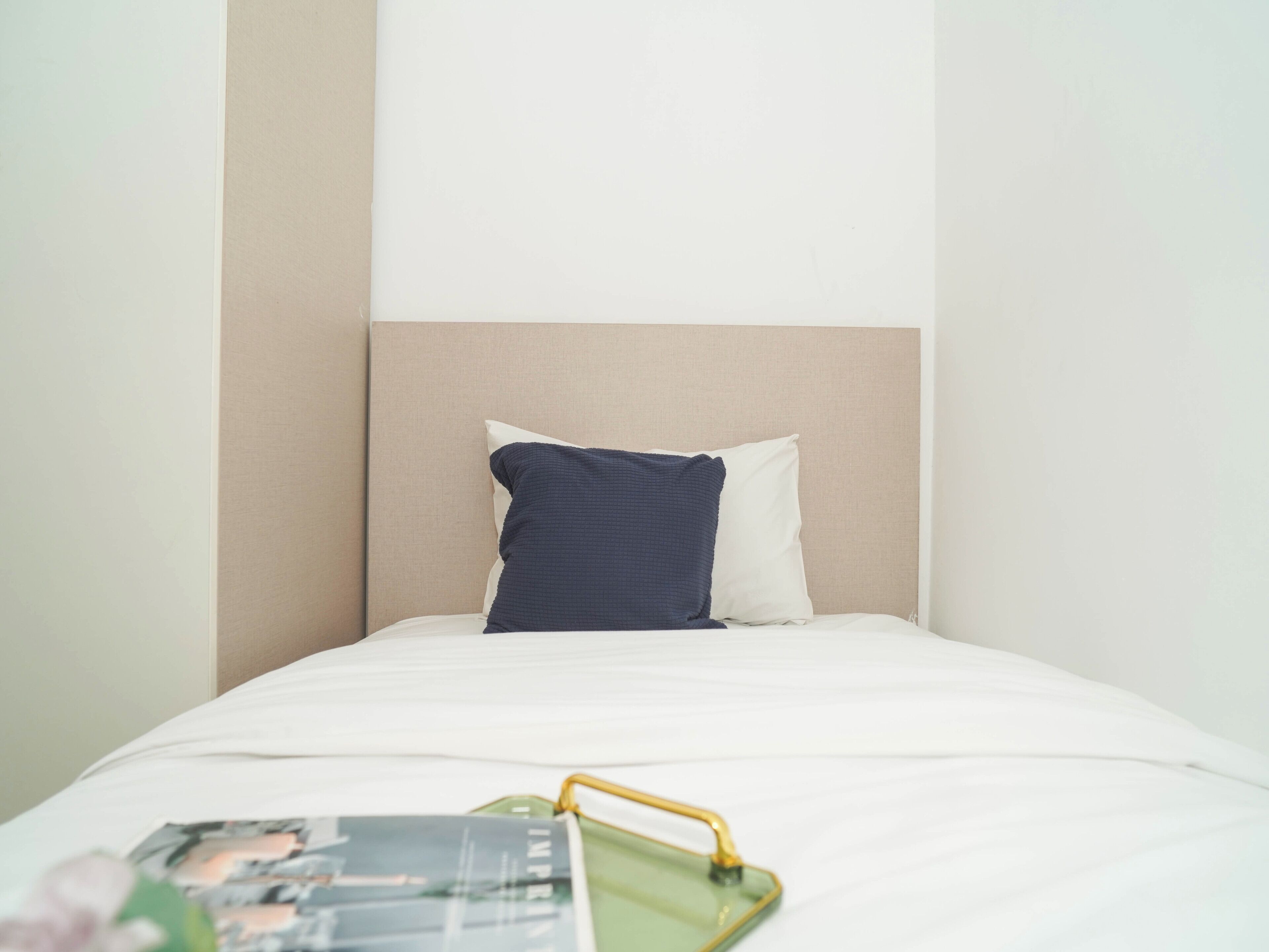 A bed with a white mattress, a beige headboard, and a dark blue pillow.