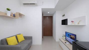 A modern living room with a grey sofa, yellow cushions, a flat-screen TV, a cabinet, and a wall-mounted air conditioner.