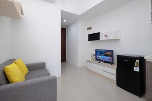 Ein modernes Wohnzimmer mit einem grauen Sofa, einem Flachbildfernseher, einem schwarzen Kühlschrank und einem weißen Schrank.