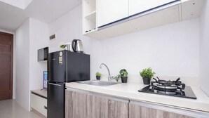 A modern kitchen with a black refrigerator, a sink, a stove, and wooden cabinets. - 2 Pax Practical 1Br At Vittoria Residence (Jakarta)