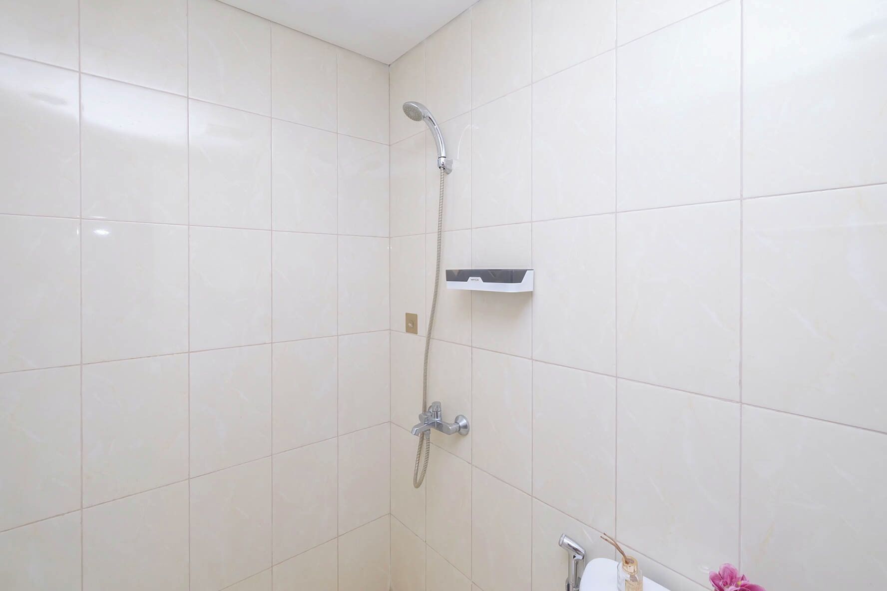 A bathroom with white tiles, a shower with a handheld showerhead, a soap dispenser, and a toilet.