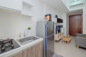 A compact kitchen with a sink, stove, and refrigerator, a small wooden side table, and a grey sofa in a living area. - Functional 2Br Apartment At Vittoria Residence (Jakarta)