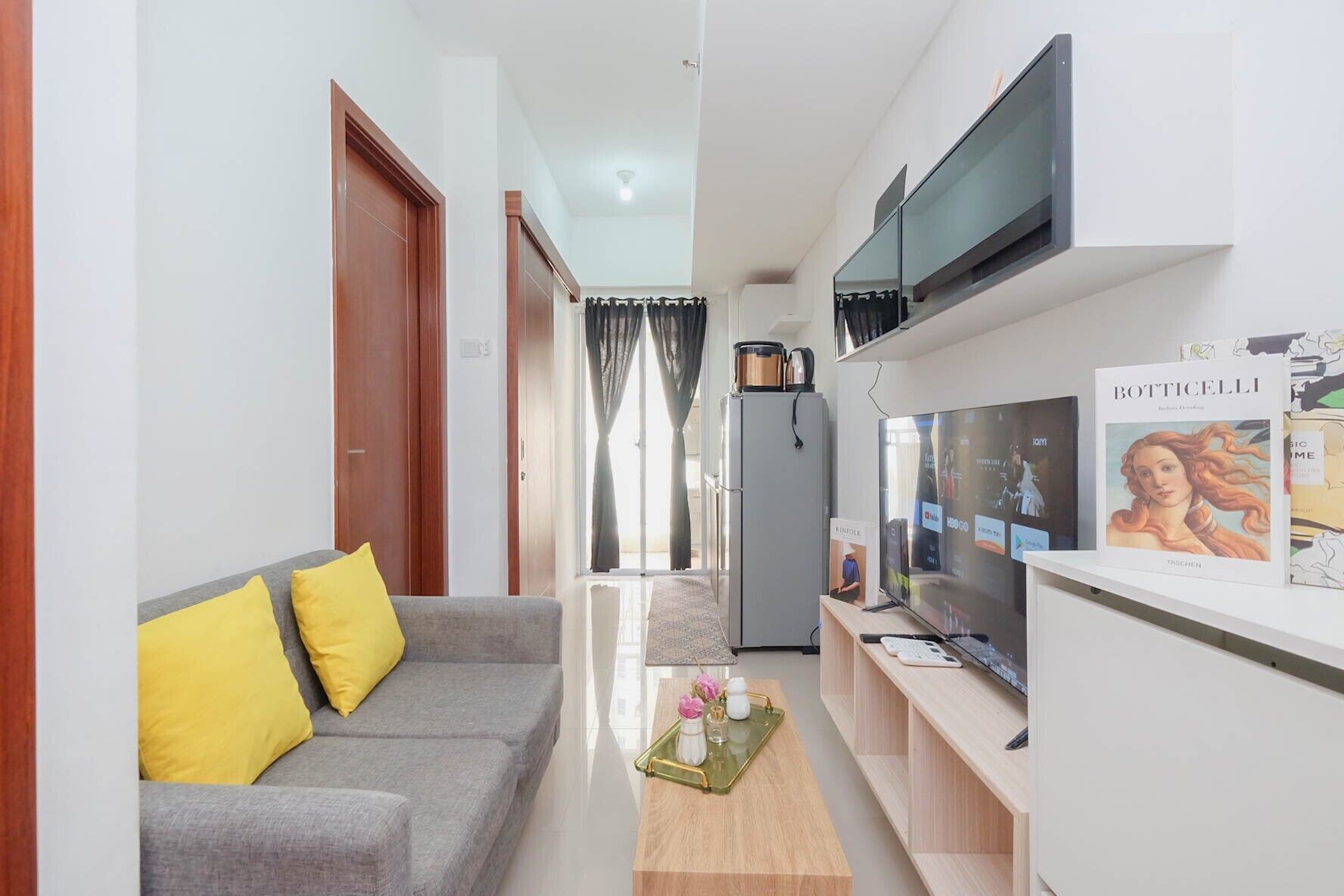 A modern living room with a grey sofa, yellow cushions, a coffee table, a TV, and a refrigerator.
