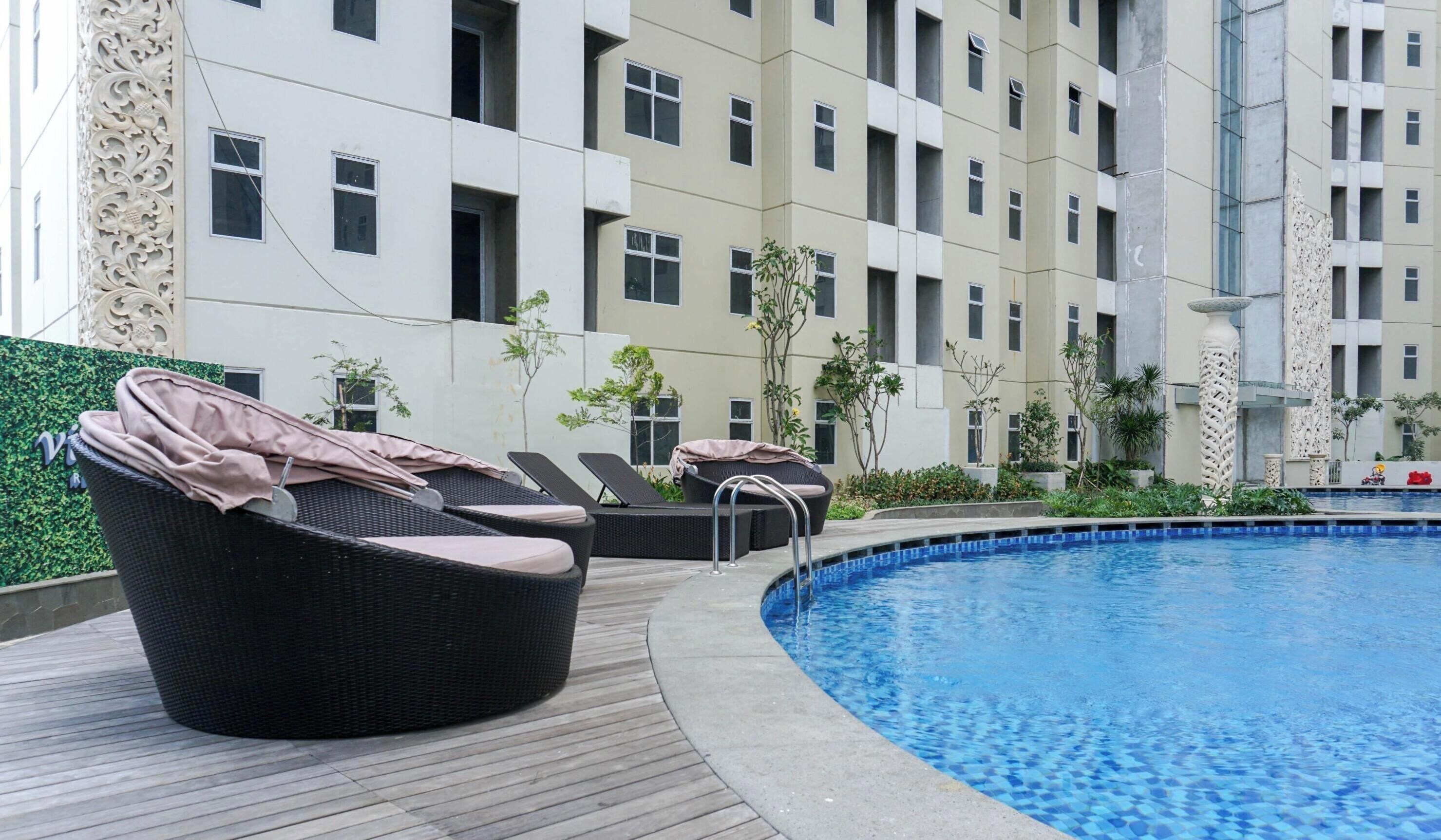 A poolside area with lounge chairs, a swimming pool, and a building with multiple windows and balconies.