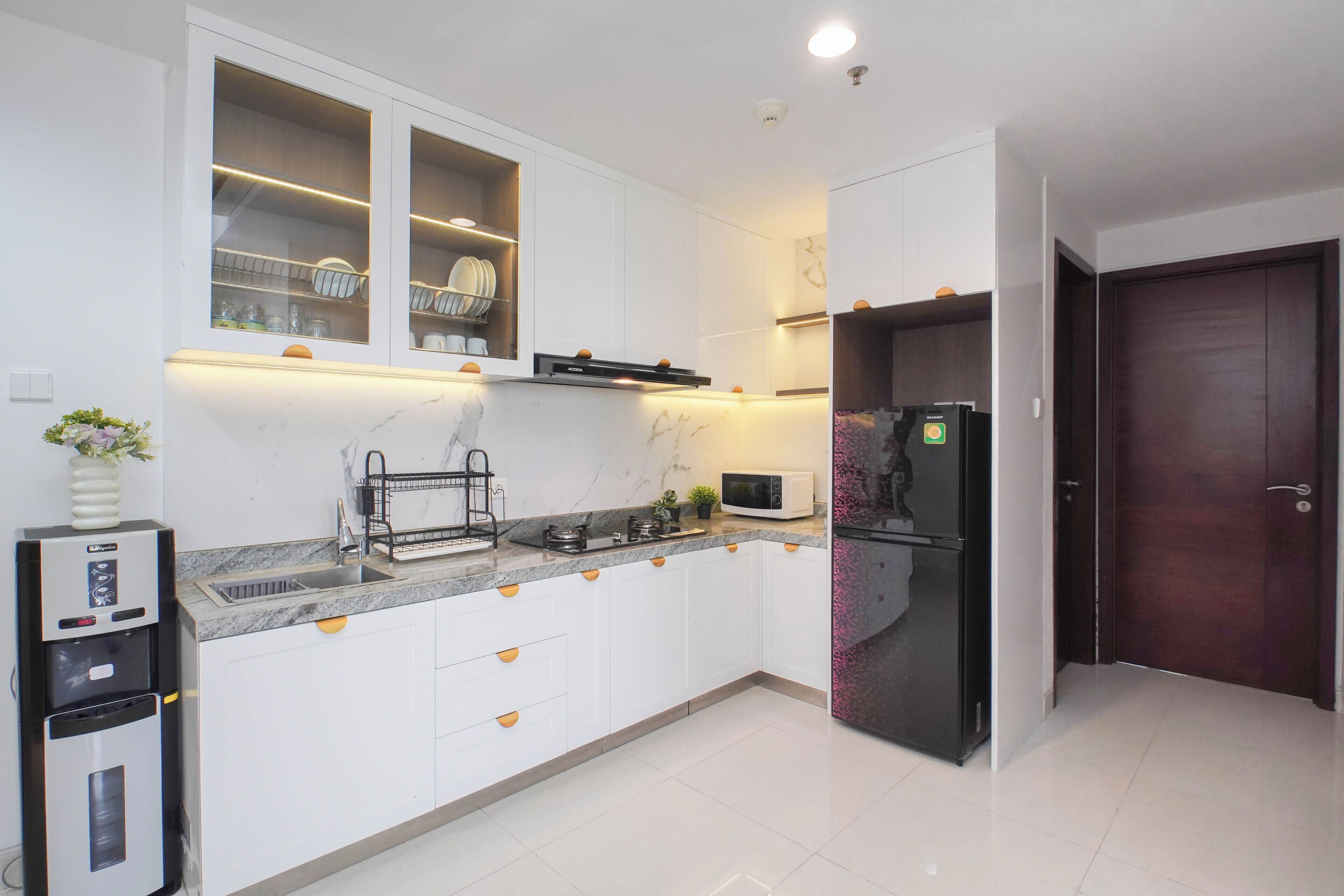 A modern kitchen with white cabinets, a built-in microwave, a refrigerator, and a water dispenser.
