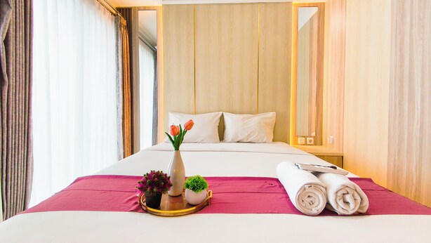 A hotel room with a bed, a bedside table with a vase of flowers, a small potted plant, and rolled towels. - Modern Style Studio At Westown View Surabaya Apartment (Surabaya)