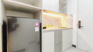 A compact kitchen with a stainless steel refrigerator, a marble backsplash, and a small countertop with a sink. - Stylish Light Gray Touch Studio At Westown View Surabaya Apartment (Surabaya)